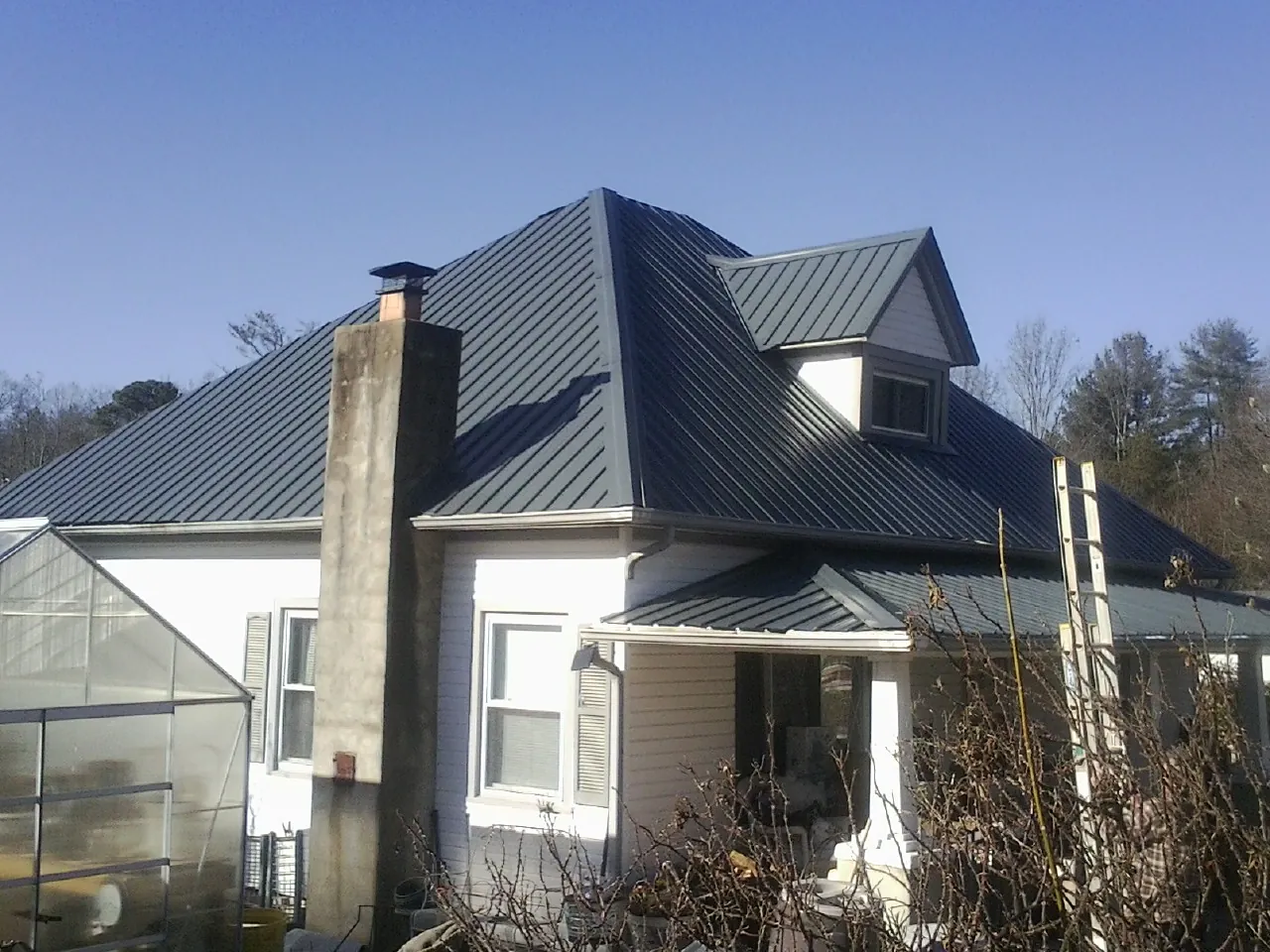 Dark blue standing seam metal roof on a white farmhouse with dormer — Slate & Tile Roof Repair by Roofing Brothers in Amityville