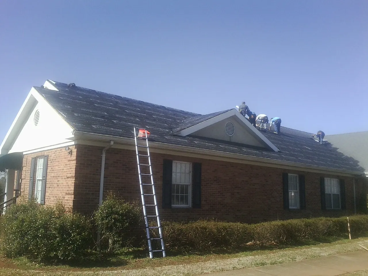Crew tearing shingles off a brick ranch roof with a ladder set — Metal Roof Repair work by our crew in Amityville
