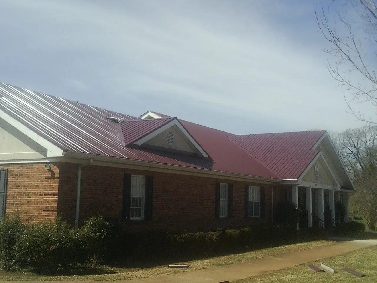 Red metal roof with gabled entries on a long brick building, from a Hail Damage Roof Repair job in Amityville