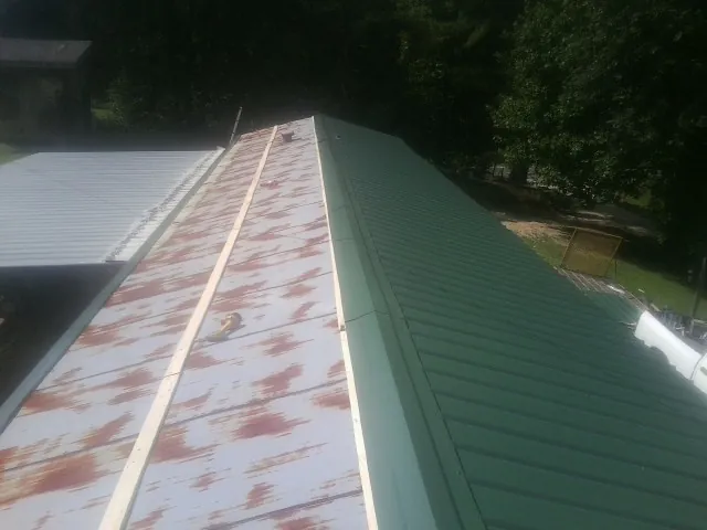 Old rusted panels beside newly installed green metal roofing — Wind Damage Roof Repair by Roofing Brothers in Amityville