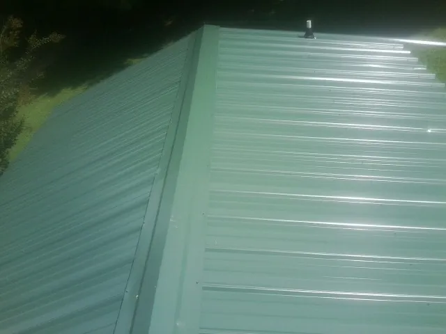 New green metal panels meeting at the ridge of a roof — Flat Roof Repair work by our crew in Amityville