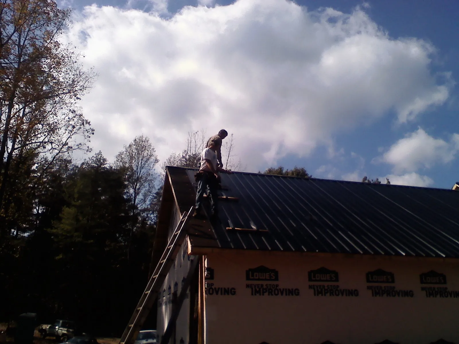 Roofer fastening dark metal panels high against a cloudy sky, from a Roof Inspection job in Amityville