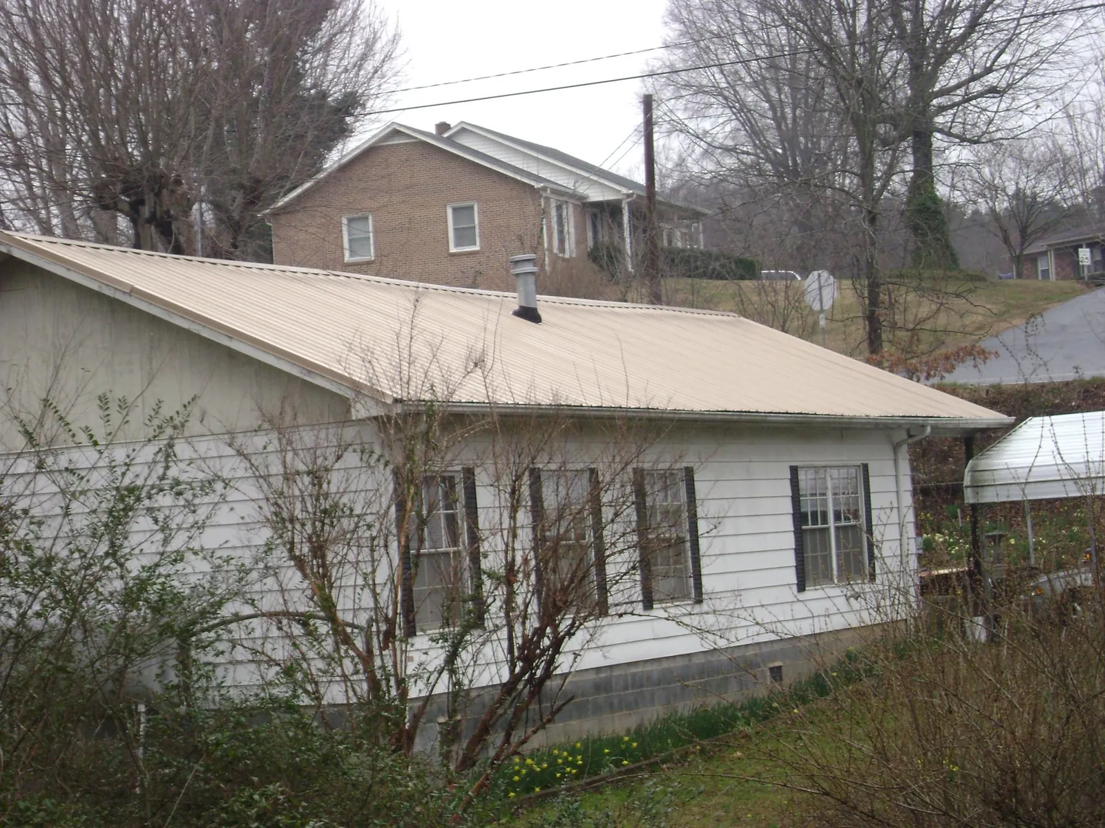 Tan metal roof on a white sided house set into a hillside — Commercial Roofing by Roofing Brothers in Amityville